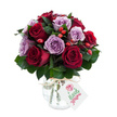 A lush, hand-gathered bouquet built around a romantic pairing of deep crimson and soft lavender roses, each bloom fully unfurled to reveal velvety, layered petals. The arrangement reads as a dense, rounded dome: about equal measures of rich burgundy and true red roses sit shoulder to shoulder with mauve-lilac varieties, their cool purple tones softening the heat of the reds. Dark, glossy foliage - likely Ruscus or Salal - creates a shadowy, supportive backdrop, the leaves' smooth sheen and slightly leathery texture giving each bloom room to breathe. Scattered through the spray are small, bright red-orange rose hips that introduce a lively, rustic punctuation; their taut skins and tiny stems offer a contrasting firmness against the roses' satiny softness. The bouquet is set into a reflective mercury-effect glass vase with an antique silvered mottle, rounded at the base and tapering at the neck, a length of natural raffia tied casually around the throat for a handcrafted finish. A plain rectangular white tag hangs from the raffia, bearing a simple floral illustration rather than a logo, and tilts forward in the light. Photographically, the composition sits on a brilliant white background that heightens colour saturation and brings out the vase's subtle gleam. The overall aroma suggests a gentle, fresh rose perfume cut with a faint, earthy green note from the foliage - a bouquet that feels both elegant and intimately familiar, ideal as a romantic gift, an anniversary surprise, or a thoughtful delivery to brighten a Stanmore home or a table after a stroll through Canons Park.