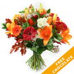 A hand-tied, seasonal bouquet that feels like an autumn walk through Stanmore Common: trumpet-shaped orange lilies open wide with visible stamens, a scattering of closed lily buds promising more blooms, and round gerbera daisies in ruby red and bright orange smiling from the center. Creamy white lisianthus with ruffled edges soften the palette, while delicate star-like astrantia with pinkish-purple hearts add fine, almost lacy texture among the blooms. Deep green foliage-likely ruscus or salal-creates a glossy, verdant backdrop and supports the composition; the stems are neatly gathered and tied with dark twine or raffia, giving the bouquet a rustic, hand-crafted finish. Most striking are the large, deeply lobed oak leaves woven through the arrangement, their burnt orange and reddish-brown tones echoing fallen leaves along Stanmore Hill and framing the flowers with autumnal drama. The lighting is clean and bright against a pristine white background, which highlights petal textures, the gentle sheen of the foliage, and the bouquet's layered depth; you can almost sense the faint spicy scent of lilies mingled with fresh greenery. In the lower right corner a bright orange diagonal banner overlays the image, clearly showing the words FREE CHOCOLATE in bold white letters, a visible promotional accent that accompanies this floral gift. This arrangement reads as a warm, welcoming present for a fall birthday, a Thanksgiving table, or a cosy anniversary, and reflects the careful craftsmanship of a local Stanmore florist who knows how to translate the season into colour and texture for same-day delivery across the neighbourhood.