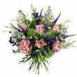 Captured from a slightly overhead angle against a bright white background, this hand-tied bouquet glows with a harmonious mix of soft pinks, mauves, deep purples and lively greens, echoing the gentle elegance of Stanmore's leafy avenues. The eye is first drawn to the pastel pink roses clustered through the centre: some are still shy, their petals cupping inward, while others are more open, spiralling beautifully to reveal subtle gradations of pink that soften toward the edges. Cocooning these roses, generously ruffled carnations in dusty rose and mauve add pillowy volume, their intricate frills giving the bouquet a plush, almost romantic vintage feel. Through this cushion of blooms, slim Veronica stems in a rich indigo-violet stretch upwards, introducing a sense of movement and vertical grace, like small floral exclamation points. Between them rest deep purple lisianthus flowers and buds, adding a velvety richness that deepens the overall palette without overpowering it. Laced throughout the bouquet, a haze of aster-like blossoms in delicate lavender-blue, each with a soft central eye, brings a gentle, whimsical texture, reminiscent of wildflower meadows glimpsed near walking paths around Stanmore. Embracing all of this colour is a varied cloak of greenery: bright chartreuse textural filler that pops cheerfully against the purples, and smooth, softly curved eucalyptus leaves in muted green, offering cool contrast and structure. The stems are neatly aligned and tightly bound at the base, showcasing the hand-tied technique that a local florist might prepare just before a delivery. Overall, the bouquet feels like a tender, uplifting gesture-perfect for birthdays, anniversaries or simply sending a moment of beauty to someone special in Stanmore.