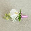 A refined white orchid boutonniere rests horizontally on a softly textured, oatmeal-coloured linen surface, captured in gentle, even light that feels like a calm Stanmore morning before guests arrive at a wedding venue. At the centre of the design, a single Phalaenopsis orchid bloom opens in pure, velvety white, its broad petals curving outwards to frame a delicately detailed throat washed with soft yellow and the faintest trace of blush pink. Around its base, tiny tufts of cloud-like white Gypsophila, or baby's breath, cluster in airy sprays, creating a halo of softness that contrasts with the orchid's smooth, sculptural form. Slim, vibrant green leaves tuck discreetly behind the flowers, adding a fresh, botanical edge without disturbing the design's clean lines. Off to one side, two tightly closed, pale lime-green orchid buds extend on a small stem, suggesting new blooms yet to open and a quiet sense of future moments and memories. The stems are neatly gathered and bound in a slim wrap of bright fuchsia pink satin ribbon, tied into a small, elegant bow whose glossy sheen catches the light and adds a celebratory pop of colour against the neutral fabric. The overall mood is one of understated luxury and timeless romance, the kind of handcrafted detail a groom or prom guest might wear to a ceremony near Stanmore Country Park or a reception along The Broadway, where fresh, thoughtfully composed flowers bring a gentle, personal touch to formal attire.