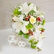 A romantic white and green floral arrangement is showcased on a smooth white tabletop, its design finely balanced between classic elegance and modern style, much like many homes in Stanmore. The flowers are nestled in a round white wicker basket, where the tightly woven strands create a gentle, natural texture beneath the blooms. Tall white lilies dominate the upper portion, their large, trumpet-shaped petals flaring outward to expose speckled interiors and rich golden stamens, as if releasing a sweet, comforting scent into the softly lit room. Close to the top centre, a single cream-ivory rose adds warmth and intimacy, its petals curled in a perfect spiral that draws the eye. Flowing from the right-hand side, a cascade of white phalaenopsis orchids tumbles gracefully down, each orchid blossom smooth and luminous, forming a delicate waterfall that would look at home at a Stanmore wedding reception or engagement celebration. Surrounding these focal flowers, bright green pom-pom dianthus and a mix of lush foliage, from feathery fronds to broader leaves, build volume and depth, echoing the layered greenery seen around Bentley Priory and Stanmore's gardens. Tiny white gypsophila blooms scatter like soft mist throughout the design, while clusters of glossy red berries inject small, vivid accents of colour, adding a festive, joyful touch. To the left of the main arrangement, two white wicker spheres rest lightly on the table, their open, interlaced pattern mirroring the basket and helping to unify the scene. The beige, linen-textured background provides a calm, neutral setting that lets the crisp whites and bright greens shine. This composition feels serene yet celebratory, ideal as a wedding table arrangement or sophisticated centerpiece for special gatherings in Stanmore.