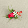 At the centre of this refined boutonnière is a striking magenta-pink rose, its petals smooth and plush, curling inward in tight concentric layers that create a sense of depth and luxury. The rose is framed by a neat arrangement of greenery, where deep green leaves sit at the base and longer, reed-like blades sweep upward and outward, giving the piece an elegant, elongated silhouette. These slender greens add a light, modern outline, balancing the fullness of the rose and making the design ideal for formal wear at weddings and celebrations around Stanmore, from local registry offices to receptions tucked near Bentley Priory. Threaded among the foliage are dainty sprays of white gypsophila, whose many tiny blossoms gather into airy clusters. They lend a misty, almost ethereal quality, softening the contrast against the vivid central bloom and bringing a hint of old-fashioned romance. The stem is securely bound in a glossy red ribbon that wraps in precise, even coils, creating a polished finish that looks both festive and refined. The ribbon's bright red hue introduces a lively spark of colour that suggests happiness and heartfelt emotion, without overpowering the delicate details of the floral work. The backdrop is understated and textured in a neutral tone, allowing the eye to rest entirely on the boutonnière: the interplay of pink, white, green, and red; the different textures from velvety petals to feathery foliage; and the overall sense of careful artistry. One can imagine this piece being prepared in a Stanmore florist's studio in the morning, then delivered fresh the same day to a waiting groom, where the light fragrance and thoughtful design will accompany every photograph and special moment.