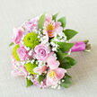 Captured from above against a soft, neutral backdrop, this bouquet appears as a carefully composed piece of floral art, full of romantic pinks and bright greens. Several pastel pink roses form the heart of the design, each bloom opening in a smooth spiral that draws the eye inward and suggests tenderness and devotion. Between them, lime-green button chrysanthemums provide playful bursts of colour and texture, their small, spherical heads offering a crisp contrast that energises the arrangement. Pink alstroemeria arc gracefully through the bouquet, their petals streaked with deeper pink and flecked with golden tones, adding a sense of movement and delicate intricacy. Tiny white flowers of baby's breath weave around the larger blossoms, colouring the spaces between them with a soft, cloud-like haze that brings lightness to the whole composition. Around the outer edges, rich green foliage cradles the blooms, giving a lush, full silhouette that feels both natural and expertly arranged, much like a bouquet prepared in a Stanmore florist studio just off the high street. The stems are bound together with a sleek magenta satin ribbon, its sheen and deep pink colour visible along the right side of the image, lending a refined finish and echoing the romantic mood. Bathed in gentle, even light, every petal, leaf, and bud is clearly defined without distraction. This bouquet would suit a wedding at a Stanmore venue, a proposal dinner at a local restaurant, or a surprise delivery to a home overlooking Bentley Priory Nature Reserve. It conveys joy, affection, and an understated elegance that works beautifully for many special occasions.