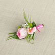 A single pink rose sits proudly at the centre of this boutonniere, its petals unfolding in soft spirals that move from a richer, cool-toned pink at the heart to a lighter, near-sheer blush at the edges. It is cradled by pale pink alstroemeria, each flower with slim, gently curving petals and a touch of yellow at the throat, streaked with fine, natural lines that add texture and visual interest. Tiny white gypsophila blossoms are threaded throughout, their cloud-like clusters forming a delicate, airy frame around the rose and alstroemeria. Wisps of greenery-slender leaves and feathery fronds-extend from behind, lending a touch of garden freshness that feels right at home in leafy Stanmore, reminiscent of morning walks near Stanmore Country Park or along quiet residential avenues. The stems are tightly bound with a glossy, satin-finish pink ribbon, carefully wrapped to create a neat, uninterrupted band that speaks to the florist's precise craftsmanship. Resting on a softly textured piece of fabric, perhaps a neutral-toned linen, the arrangement is set against a backdrop that highlights the pastel colours and gentle curves of each petal. The lighting is even and calm, without sharp shadows, giving the boutonniere a serene, timeless quality-ideal for a groom's lapel, a best man, or a special guest at a wedding or formal event in and around Stanmore. You can almost feel the cool touch of the ribbon and the smoothness of the rose, and imagine a faint, fresh fragrance that lingers just long enough to mark the moment as something cherished and meaningful.