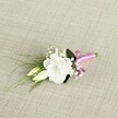 A delicately crafted wedding boutonniere rests diagonally across a softly textured, light beige fabric that looks like finely woven linen, its natural oatmeal tones giving the image a warm, calm backdrop. At the centre of the arrangement sits a single white lisianthus bloom, fully open and perfectly formed, its many ruffled petals curling gently like soft waves of silk. The flower's creamy heart fades out to crisp white edges, creating a serene, luminous focal point. Just to the left, two slender lisianthus buds in pale cream and fresh light green are tucked closely beside the main bloom, their smooth, closed petals suggesting flowers that will open later in the day, perhaps just in time for the ceremony. Clusters of tiny white gypsophila are interlaced among the blooms, each airy cloud of baby's breath catching the light and adding a sense of movement and softness. Threads of fine, grass-like greenery sweep out towards the lower left, contrasting with the broader, deeper green leaf that cradles the back of the lisianthus, grounding the design. At the base, the neatly aligned stems are wrapped in a vibrant fuchsia pink satin ribbon, tied into a small, jaunty bow that provides a cheerful splash of colour against the neutral background. The satin catches the light with a subtle sheen, hinting at celebration and joy, much like a summer wedding around Stanmore Country Park. Photographed from a slightly raised angle with gentle, even lighting, the image highlights each texture-from petal to fabric-evoking the feeling of holding this small, elegant accessory just before pinning it to a lapel for a wedding or prom in Stanmore.