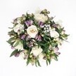 Viewed directly from above against a pure white background, this hand-tied bouquet forms a soft, almost perfect circle of creamy whites, deep purples, and rich greens, like a little garden floating in mid-air. At its heart sit several creamy white roses, their petals spiralling outwards in tight, velvety layers that shift gently from ivory to pale champagne. Some blooms are fully open, showing their intricate centres, while others remain more cupped, suggesting the promise of further unfolding. Threaded between the roses are clusters of Alstroemeria buds in dusky lavender, plum, and magenta, their outer petals flushed with colour but tipped in fresh green, as though just picked from a shaded corner of a Stanmore garden near Bentley Priory Nature Reserve. Tiny clouds of white gypsophila hover delicately throughout, their fine stems and miniature blossoms softening the stronger tones and giving the whole design a dreamy, almost weightless quality. Deep emerald foliage, broad and slightly glossy, encircles and supports the flowers, with leaves peeking through at different angles to create depth and gentle movement. The lighting is even and natural, with no harsh shadows, allowing every detail-the satin-like rose petals, the firmer texture of the Alstroemeria buds, the feathery baby's breath-to be clearly seen. The bouquet feels calm and reassuring, suited to moments of quiet congratulations, tender sympathy, or intimate celebration at home in Stanmore. Its refined, balanced palette and careful craftsmanship speak of elegance and serenity, like a peaceful pause in the middle of a busy day along The Broadway.