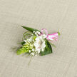 This beautifully composed floral boutonniere lies on a softly woven, oatmeal-coloured fabric, the neutral background allowing every botanical detail to stand out with clarity, much like the way soft light brings out the textures of Stanmore's leafy streets. At its heart is a white alstroemeria, fully open yet delicately shaped, each petal smooth and luminous, adorned with fine reddish-brown flecks that provide subtle contrast without disturbing its purity. Around it, smaller white blooms and buds-reminiscent of campanula or lily-of-the-valley-cluster closely, some still closed, others just beginning to reveal their petals, giving the arrangement a feeling of quiet unfolding. Wisps of baby's breath are interlaced throughout, their tiny white blossoms adding a cloud-like softness and an almost ethereal aura. On the left side, a striking, elongated cluster of vivid green Ornithogalum buds forms a textured cone, bringing a modern, structured note that pairs well with the softer flowers. Behind and beneath the blooms, broad, dark green leaves provide shape and stability, while long, slender strands of bear grass curve gently outward, suggesting movement, as though stirred by a light breeze drifting across Stanmore Country Park. The stems are neatly bound with a glossy pink satin ribbon, tied into a neat bow that catches the light and contributes a sweet, celebratory touch. The arrangement feels intimate and intentional, ideal for pinning to a groom's jacket, a prom suit, or a special occasion outfit in Stanmore, a small floral accent that conveys sincerity, freshness, and a refined sense of style.