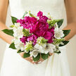 This elegant bouquet, likely photographed against a soft, neutral backdrop similar to the calm interiors of homes around Stanmore Hill, draws the eye first to its luxurious magenta peonies. These central blooms are plush and rounded, made up of countless petals that fold and curl inwards, creating shadows and depth that give the flowers a velvety, almost cloud-like appearance. Surrounding them, white alstroemeria spread their long, graceful petals, each one adorned with fine burgundy striations that radiate from the centre. These markings add a gentle note of drama, tying the pure white tones back to the deeper pinks at the bouquet's core. Rising from among the blossoms are slender green spikes and shy buds, their upright shapes and fresh colour suggesting new beginnings-much like the emerging leaves that line the paths toward Stanmore's Jubilee Line station in spring. The bouquet is wrapped in an embracing halo of greenery, where smooth, substantial leaves blend with more delicate foliage, giving structure and a sense of movement around the edges. Natural light glides across the arrangement, accentuating the softness of the petals and the slight sheen of the leaves, so the bouquet appears vivid and three-dimensional. Imagining the scent, you might think of clean stems, a gentle floral sweetness, and a whisper of earthiness, like gardens waking up along Dennis Lane after a cool evening. This bouquet feels tailored for a Stanmore bride who loves understated luxury, or for couples celebrating an engagement dinner at home. It's a composition where every element-colour, shape, and texture-comes together to create a quiet, confident expression of romance and hope.