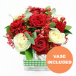 Captured against a simple white backdrop, this bouquet radiates the warmth and intimacy of a carefully planned celebration. At its heart, full red roses with velvety, layered petals intertwine with creamy white roses whose soft tones bring a calm, luminous contrast. The traditional pairing of red and white creates an atmosphere of romance and devotion, perfectly suited to a quiet evening at home in Stanmore, perhaps after a stroll near Stanmore Country Park. Fine tufts of tiny red filler flowers, similar to dyed gypsophila, drift through the arrangement in airy clusters, giving a feeling of lightness and motion, as though the bouquet were gently breathing. Among them, plump red hypericum berries nestle like tiny polished marbles, their glossy surfaces reflecting the light and adding little points of festive sparkle. Surrounding the central blooms, eucalyptus leaves and fresh green foliage reach outward and upward, adding volume, texture, and a suggestion of a clean, refreshing scent. The flowers are gathered in a sleek rectangular glass vase, the clear sides showing the neatly aligned stems and clean water inside, reinforcing a sense of freshness and care. Around the centre of the vase, a green and white gingham ribbon is wrapped in a neat band, bringing a homely, rustic detail that would sit beautifully on a Stanmore kitchen counter or as a centrepiece for a family celebration. In the bottom right corner of the image, a standout orange circular emblem carries the words VASE INCLUDED in bold white type, clearly indicating that the arrangement arrives complete and ready to place. The overall effect is of a thoughtful, ready-made gift, ideal for anniversaries, Valentine's Day, or sending love and appreciation to someone special in and around Stanmore.