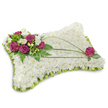 A rectangular pillow-shaped sympathy tribute rests on a clean white backdrop, its surface densely carpeted with hundreds of small, pure white chrysanthemum florets that read like a soft, cloudlike texture beneath the eye. The chrysanthemums' tightly packed petals create a tranquil, matte surface that suggests quiet rest; a faint shadow beneath the cushion anchors it to the space and gives the design a gentle presence. In the upper-left corner a compact, vibrant cluster of deep magenta-fuchsia roses creates an immediate focal point-their velvety petals unfurling with rich colour-while small white freesia or lisianthus blooms peek between them, adding delicate points of brightness and a whisper of citrus-vanilla fragrance. Fresh green foliage, including feathery fern fronds and smaller glossy leaves, frames the cluster and provides a cool, living contrast to the white chrysanthemum field. From that floral weight, two or three long, linear stems of bright green bear grass sweep in elegant arcs across the pillow, guiding the eye toward a solitary magenta rose placed near the lower-right corner, which balances the composition with a considered single-stem gesture. Around the entire edge, a folded lime-green satin ribbon is pleated into a neat scalloped trim, its subtle sheen catching the light and outlining the cushion with a refined, finished look. The craftsmanship reads as timeless and consoling-an arrangement chosen to express sympathy, peace, and remembrance. As a florist familiar with Stanmore's quiet streets and nearby Canons Park memorials, I picture this tribute offered gently at a funeral service, where its soft colours and textures give comfort and a visual pause for reflection.