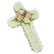 In the photograph, a reverent floral cross stands upright against a spotless white background, its faint shadow softly outlining its form. The cross follows the familiar Christian shape, with gently widened arms and a long vertical stem, and is completely covered in tightly packed white button chrysanthemums. These small, round blossoms create a rich, textured surface, their overlapping petals forming a seamless sea of white that feels calm and soothing to the eye. Around the perimeter, a fine band of lime green ribbon forms a delicate frame, peering out from under the chrysanthemums and giving the cross a defined, polished edge and a quiet breath of colour. At the very centre, where the cross's beams meet, a graceful cluster of accent flowers adds depth and warmth. Here, open roses in soft shades of blush pink, creamy white, and pale peach are nestled together, their petals layered and slightly cupped, suggesting affection, tenderness, and cherished memories. Slender fern fronds and tiny lavender or lilac filler blossoms emerge from between the roses, introducing hints of green and pale purple that lend visual contrast without overpowering the serene design. The overall composition appears carefully balanced and thoughtfully crafted, ideal as a floral tribute for a funeral or memorial gathering in Stanmore, whether placed near a coffin, beside a framed photograph, or at a graveside. It captures the spirit of quiet respect and faith, reflecting the kind of piece that might be lovingly arranged by Flower Delivery Stanmore for local families seeking a dignified symbol of condolence and hope.