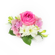 A compact, elegant corsage arranged on a pristine white background, shaped to read like a small love letter in flowers. The focal bloom is a lush bubblegum-fuchsia rose, its inner petals tightly swirled and velvet-soft, opening outward to display subtle shifts of pink and magenta. Around it, airy clusters of pale pink and lavender hydrangea create a soft, cloud-like halo, their tiny florets adding a gentle volume and a romantic, vintage touch. Scattered among the pastel blooms are creamy white, trumpet-shaped alstroemeria or small lilies, each with a green-tinged throat that brightens the centre and lends a cool, clean contrast to the warm rose. Deep, glossy green leaves sit at the base and edges, broad and slightly waxy to the touch, giving the composition weight and a natural frame. Slender, upward-reaching green buds with hints of yellow promise future blooms and introduce a fresh, hopeful vertical movement. A delicate cluster of pearlescent beads cascades at one side, catching the soft studio light and adding a refined, heirloom sparkle reminiscent of a bride's pearl bracelet. The lighting is bright and natural, revealing the petals' velvety textures and the hydrangea's faintly veined surfaces while suggesting the faint scent of freshly cut roses and garden leaves. This compact arrangement feels perfectly suited to weddings, proms, or intimate anniversary moments and would read beautifully beside local details-imagining it worn walking down Stanmore High Street or pinned for photos at Canons Park creates a quietly personal connection. A florist's hand is evident in the balanced spacing and thoughtful use of pearls to finish the look.