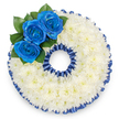 A bespoke funeral tribute crafted into the distinct shape of the number '0', shown from above against a pristine white backdrop. This memorial piece is composed of hundreds of small, tightly clustered white spray chrysanthemums that form a pillowy, continuous surface across the numeral, their delicate petals creating a soft, calming texture that suggests quiet and solace. The outer and inner rings of the '0' are traced with a pleated royal blue satin ribbon, the same vivid shade repeated like a steady heartbeat around the circumference; the ribbon's ruffled scallops cast subtle shadows that give the number a formal, framed presence. At the upper left curve a compact cluster of three royal blue roses provides a concentrated point of colour-each rose unfurls from a deep, velvety center and sits against glossy dark green leaves that push the blue forward and add a natural depth. The overall palette-pure white, deep sapphire blue, and rich green-reads as dignified and deliberate, a visual language of peace, respect, and enduring memory. This numerical tribute often marks an age or significant number at a service, personalised to the life being commemorated, and its neat craftsmanship reflects the care of experienced hands. As an east-of-Harrow florist serving Stanmore and surrounding neighbourhoods like Canons Park and Stanmore Broadway, we design these pieces with an attention to proportion and finish so they read clearly from a distance during a service. The arrangement's clean lines and tactile softness make it suitable for a chapel, wake, or graveside, offering a quiet, measured comfort to those who gather to remember.