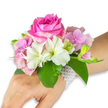 A delicate wrist corsage that reads like a soft love letter to spring: photographed on a light-to-medium skinned left hand and forearm against a clean white backdrop, it centers on a single, richly saturated deep fuchsia-pink rose whose velvety petals unfurl in a compact, spiral bloom. Around that rose, clusters of blush pink hydrangea florets build a plush, cloud-like base, their papery texture catching the light and lending airy volume. Interspersed between those blooms are several crisp white alstroemeria - Peruvian lilies - each with four to six smooth petals and faint pale green streaking at the throat, adding a refined, luminous contrast. On one side, a small cluster of pale green alstroemeria buds and a few barely open pink buds suggest gentle movement and promise of more blossoms to come. Broad, glossy emerald leaves cradle the composition, their smooth, cool surfaces framing the flowers and intensifying the pinks and whites. The whole arrangement is fastened by a multi-strand bracelet of tiny, lustrous white pearls that form a soft, net-like band around the wrist and trail slightly onto the back of the hand, giving the piece a timeless, jewellery-like quality. Soft studio light highlights the rose's depth of colour and the hydrangea's translucent edges while allowing a faint suggestion of scent - a gentle, romantic blend of fresh rose and clean florals - to be imagined. Perfect for a wedding, prom, or a first dance, this corsage balances craftsmanship and tenderness: wearable floristry designed to feel both intimate and thoughtfully composed, as might be chosen for a celebration in and around Stanmore's tree-lined streets and quiet parks.
