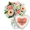Presented as if on a pristine tabletop in a Stanmore home, this Mother's Day arrangement is photographed against a bright white background that highlights its gentle colours and clean lines. A clear glass vase sits slightly to the left, its straightforward shape softened by a band of light brown twine knotted loosely around the neck, a detail that hints at the personal touch of a neighbourhood florist serving families near Stanmore Hill and Kenton Lane. The vase holds a generous bouquet of mixed blooms in warm pastel hues. Fully opened peach-pink roses reveal their spiralling centres, each petal overlapping the next like layers of silk. Interspersed among them are cheerful peach gerbera daisies, their petals forming perfect circles around deep, dark brown centres that draw the eye. Smaller white chrysanthemums with subtle green hearts and airy clusters of baby's breath fill the spaces between, creating lightness and gentle movement across the top of the bouquet. Sprigs of fresh green foliage peek through at different heights, framing the softer tones and suggesting the crisp fragrance of cut stems. Just behind the flowers, partly hidden, a small white card with blurred pink and green handwriting hints at a private Happy Mother's Day message. To the right of the vase a large, heart-shaped Mylar balloon rests against the arrangement as if leaning in for a photograph. The balloon is bright white, sprinkled with metallic gold and silver dots that mimic scattered confetti. In the centre sits a peach-coloured heart, inside which the message HAPPY Mother's DAY appears in bold black lettering, the word Mother's picked out in graceful script. The whole composition feels joyful yet calm, ideal for capturing the warmth of Mother's Day deliveries across Stanmore, Belmont and nearby Canons Park.