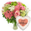 The image portrays a joyful, spring-bright Mother's Day gift set, perfectly suited to a Stanmore home celebrating a special Sunday. On the left, a clear glass vase showcases a lush, domed bouquet, its shape carefully rounded to feel full yet not overwhelming. The main blooms are pink roses, each one open enough to reveal its layered heart while still holding a gentle curve at the edges, where the colour deepens to a slightly darker pink. Around these, coral-pink clusters of small, star-like blossoms-similar to kalanchoe-add denseness and interest, their many tiny petals creating pockets of intricate texture. Popping out between the pinks, lime-green button chrysanthemums introduce a lively contrast, their compact, pompom-like heads defined by fine, frilly petals that catch the light. Interspersed among the stronger tones, white daisy-style spray chrysanthemums bring clarity and lift, their simple shapes and pale faces acting like little breaths of air within the design. Dark green foliage supports everything from below, spilling gently around the edges of the bouquet, adding structure and framing the brighter colours. The vase reveals the natural stems arranged in clear water, a quiet reminder of freshness and careful preparation. To the right, a heart-shaped foil balloon completes the composition, echoing the sentiment of the bouquet. Its white background is speckled with metallic dots in shades of gold, silver, and peach, giving a softly sparkling effect. At its centre, a peach heart surrounds the message HAPPY Mother's DAY in stylish black lettering, mixing bold and cursive fonts. The scene feels like a moment captured just before the surprise-perhaps on a kitchen counter in a Stanmore house near Canons Park-ready to delight a mother with colour, texture, and heartfelt thanks.